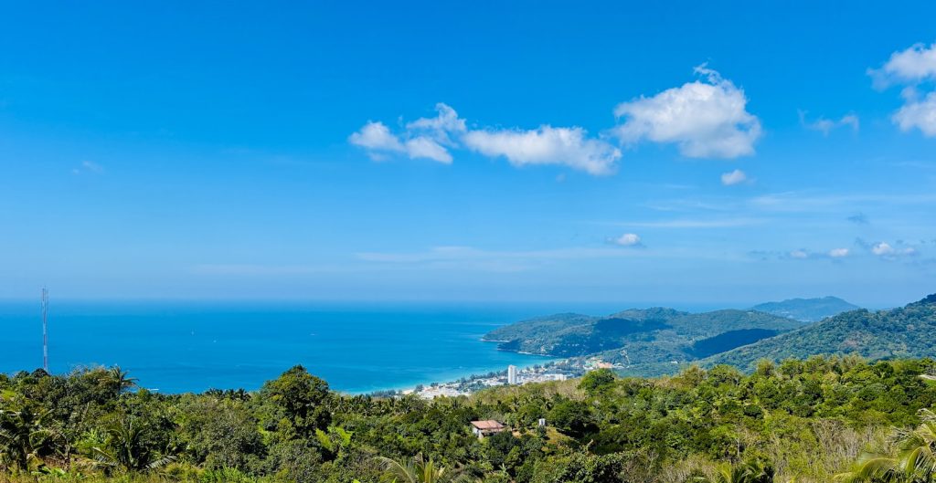 Lush green hills overlook a coastal town and blue ocean.